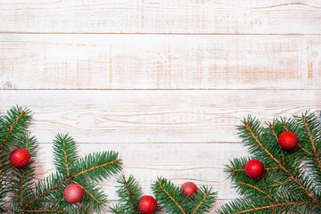 Christmas background - fir branches and red ornaments on a white wood table. Flat layout, top view composition border with copy space