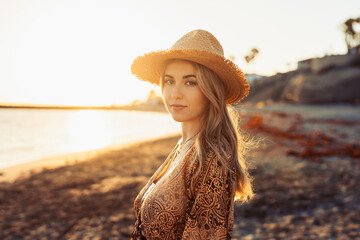 Portrait of one young beautiful woman on the sand of the beach enjoying and relaxing at the sunset of the day. Looking at the camera serious..