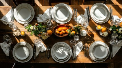 A rustic wooden dining table is set for a meal with white plates, silverware, glasses, and floral centerpieces.