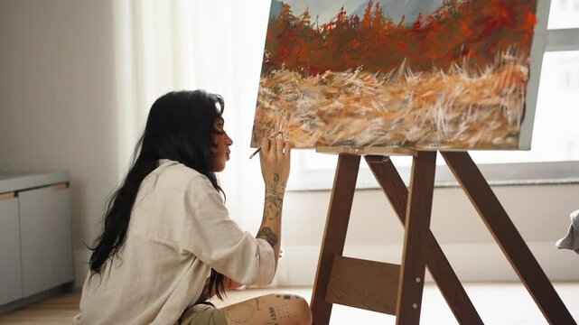 Serious transwoman female artist is working at picture using oil paints and palette-knife creating beautiful landscape on canvas. Painting technique and painters

