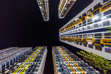 Low-angle view of colorful, illuminated high-rise buildings surrounding a dark night sky,...