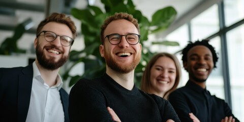 Obraz premium A group of four diverse young professionals stand closely together, laughing in a bright office, reflecting teamwork, camaraderie, and a positive workplace atmosphere.