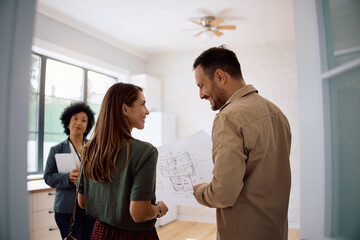 Happy couple examining blueprints while buying new apartment.