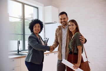 Happy couple and real estate agent shaking hands and looking at camera.