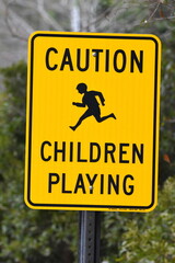 A bright yellow and black sign that says Caution Children Playing and has a picture of a child running.