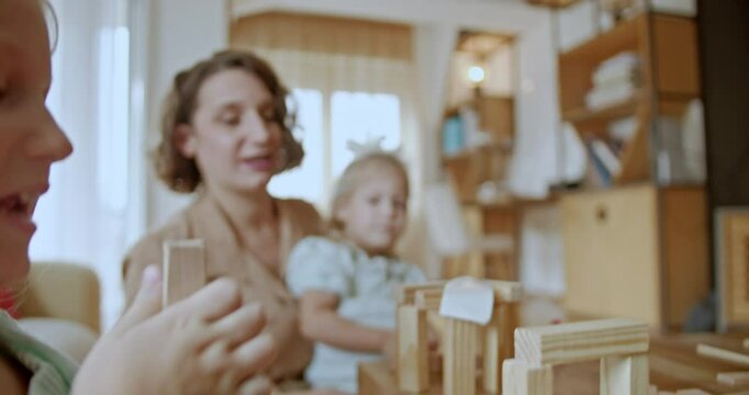 Mother and two daughters having fun playing with wooden toy blocks at home.