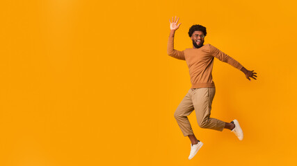 Cheerful black guy in glasses jumping over orange background