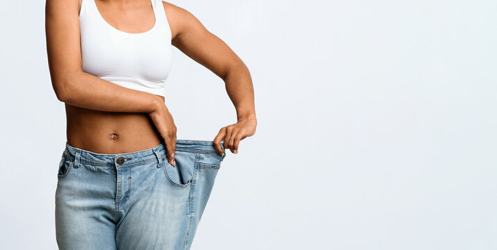 Cropped of afro woman wearing too large jeans, demonstrating weight loss, effective diet concept