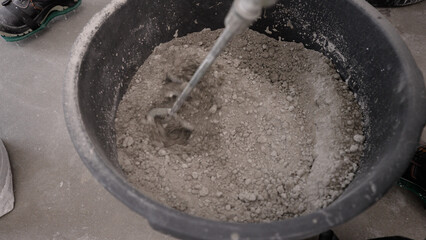 Construction worker mixing mortar with electric mixer.