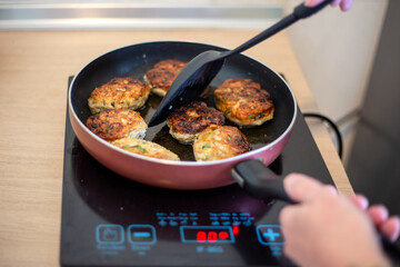 Cooking. The frying pan is on the induction stove, the hostess is turning the meat patties over to fry them.