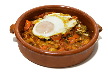 Vegetable ratatouille with a fried egg on top, served in a clay bowl. Isolated on a white background. Spanish food concept.