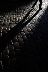 Shadow of walking pedestrian on cobblestone road
