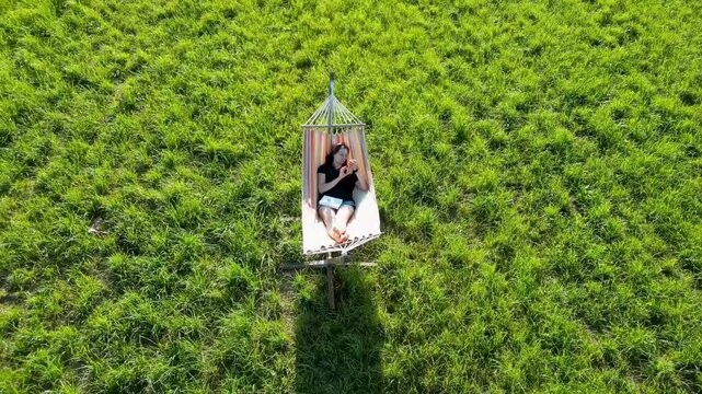 au milieu d'un champ, une femme dans son hamac qui regarde son t&eacute;l&eacute;phone portable