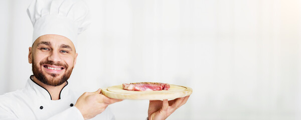 Cooking Meat. Chef Man Holding Fresh Steak On Chopping Board Smiling At Camera Standing In Kitchen Indoor. Selective Focus