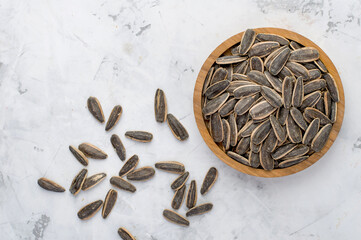 Gray sunflower seeds with salt in a wooden bowl on a light background.  Top view, horizontal.