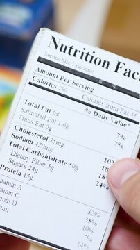 Holding food label with ingredients on paper box. Shopping and nutrition focus. Label affixed to product with printed information. Critical details provide insight into product contents and quality