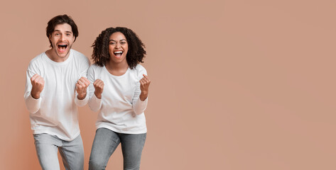 Big Win. Cheeful mixed-race couple celebrating success, raising hands with excitement over yellow...