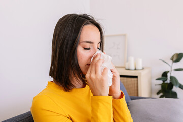 Sick young woman with common cold feeling pain blowing nose with tissue. People health care and virus infection concept