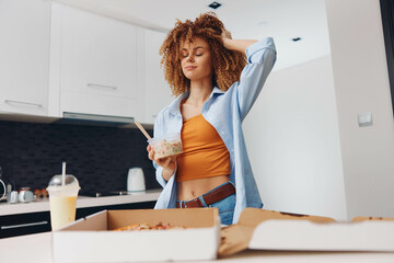 Woman with curly hair standing in front of pizza box and cup of coffee in a cozy setting