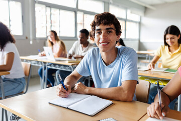 Portrait of young student boy smiling at camera while attending teacher in classroom. Education lifestyle concept