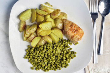 seasoned baked chicken thigh  with potatoe wedges and peas