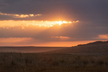 The setting sun through the clouds and reflections on the hills