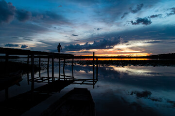 Atardecer en lago con con hombre sobre el muelle contemplando hermoso cielo azul