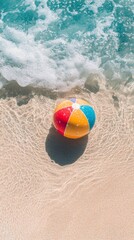 Obraz premium Colorful beach ball on sand with ocean waves, summer vacation concept