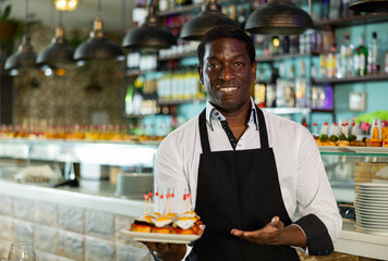View on the African adult man holding tapas at a pub with diverse group in the background