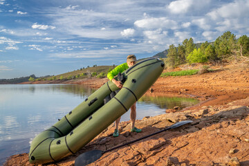 senior male paddler is adding air to an inflatable packraft on a lake shore in Colorado, summer on...