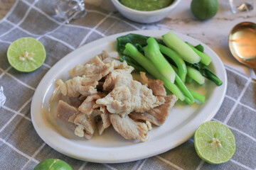 Boiled Pork with Lime Garlic, kale and Chili Sauce in white plate. Thai hot and spicy food. Healthy eating, Asian cuisine, and sustainable dining.