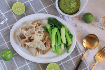 Boiled Pork with Lime Garlic, kale and Chili Sauce in white plate. Thai hot and spicy food. Healthy eating, Asian cuisine, and sustainable dining.