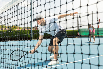 Portrait of man playing with male partner tennis doubles game on outdoors court. View through the tennis net