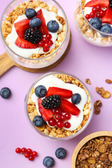 Tasty yogurt with fresh berries and granola in glasses on violet background, flat lay