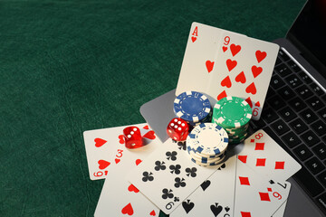 Poker chips, laptop, playing cards and dices on green table. Online game