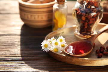 Tincture in spoon, chamomiles and dried berries on wooden table