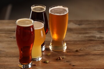 Glasses with different types of beer and pistachio nuts on wooden table