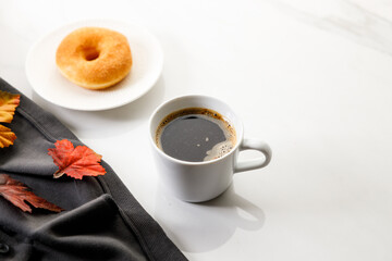 Cup of black coffee, Donut, leaves, on white marble background. Autumn composition.