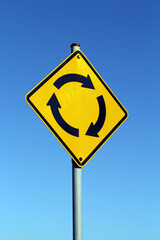 Yellow roundabout traffic circle sign against a clear blue sky background