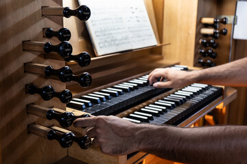 Left side view of Organist playing organ and changing Organ registers in Catholic Church.