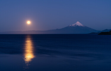 Full moon rising and reflecting on Lake Llanquihue after sunset, with the majestic Osorno Volcano in the background, viewed from Puerto Varas in the Patagonia of Chile.