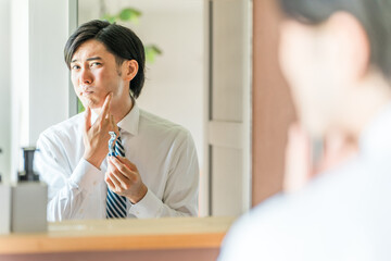朝出勤前に洗面所で髭剃りをするスーツ姿の若いアジア人ビジネスマン

