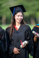 A woman in a black graduation gown holding two white graduation certificates