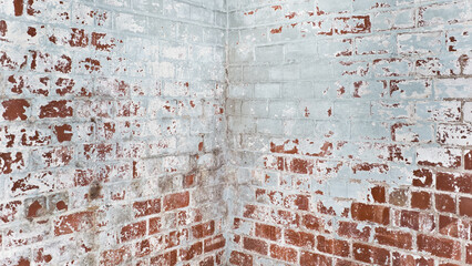 Close-up color photo of the corner of an old brick wall with peeling paint.