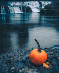 moody autumn landscape with pumpkin in front of waterfall