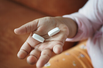A Childs Small Hand Gently Holding Two White Pills While Sitting on a Cozy Couch