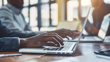 A colleague typing on a laptop while another takes notes during a discussion.