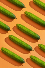 Green cucumbers on orange background arranged diagonally; ideal for food blogs, cooking websites, healthy lifestyle content, and culinarythemed designs.