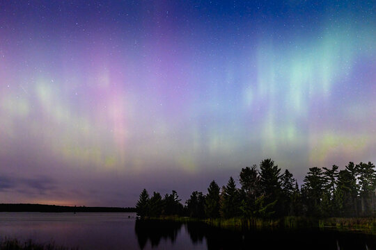 Northern lights erupt over remote Minnesota lake at night with rainbow of color shining off water Aurora Borealis nature show