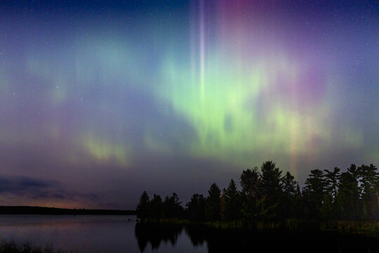 Northern lights erupt over remote Minnesota lake at night with rainbow of color shining off water Aurora Borealis nature show